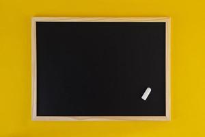 Empty black chalkboard on yellow background. Front view on black chalkboard with wooden frame. Empty copy space on flat panel. photo