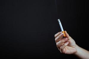 Hand holds a lighted cigarette on a dark background photo