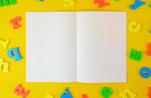 Opened two pages notebook on yellow background covered with letters. Education concept. Copy space paper for photo and text message.