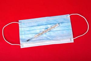 Protective medical face mask and thermometer on a red background