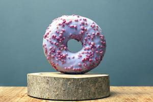 Donut with purple glaze on a wooden stand on a gray background photo