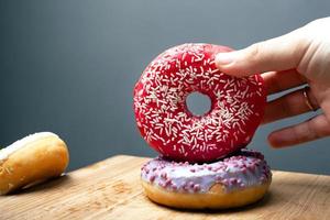 Female hand holds sweet pastry donuts with red and violet glaze on a gray background