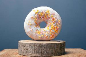 Donut with white icing and colorful powder on a wooden stand and gray background photo