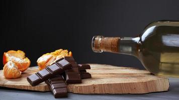 Botella de vino blanco con chocolate con leche y mandarina sobre un soporte de madera