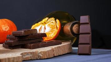 Trozos de chocolate, mandarinas y una botella de vino en una placa de madera