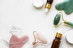 Rodillo de jade de masaje facial con producto cosmético sobre fondo de mármol blanco
