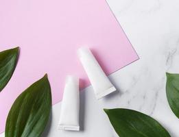 White tubes of cream on a marble and pink background photo