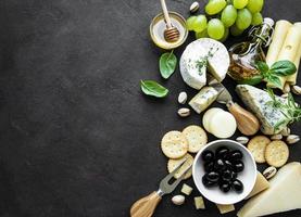 Various types of cheese, grapes, honey, and snacks on a black concrete background