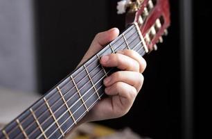 La mano del guitarrista aprieta los dedos sobre los acordes de una guitarra acústica.