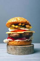 Delicious burger with a large meat cutlet with vegetables, cheese and fries on a gray background photo