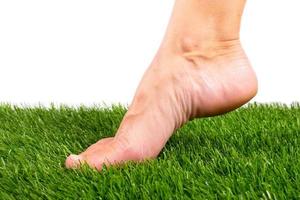 Bare foot touches green artificial grass close-up on a white background photo