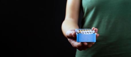 Person offer smoking, pack of cigarettes in hand on a dark background with copy space photo