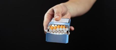 Pack of cigarettes in hand on dark background with copy space photo