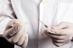 Doctor in a white coat and gloves holds opens a syringe photo