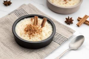 Creamy rice pudding with cinnamon in bowl on white marble table photo