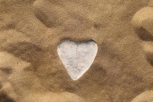 piedra en forma de corazón sobre arena. Fondo de arena de mar, papel tapiz. Día de San Valentín, boda, luna de miel o concepto de tarjeta de felicitación de amor. foto