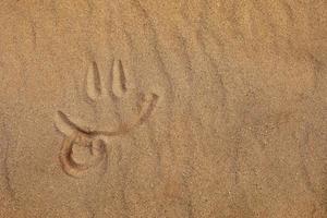 Smiley face with tongue out made by finger on a sandy beach photo