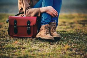 Stylish young girl in brown shoes and a warm coat sitting in the park with a red bag. photo