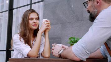 glad kaukasisk man och kvinna njuter av kaffe och ler medan du sitter på caféterrassen video