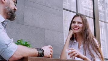 Feliz el hombre y la mujer caucásicos disfrutando de un café y sonriendo mientras están sentados en la terraza del café juntos video