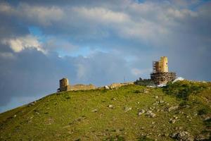 View of Genoese fortress on the side of a mountain with a cloudy blue sky in Crimea photo