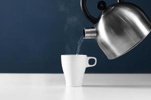 Kettle pouring boiling water into a cup with steam on wood table photo