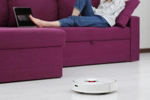 Robot cleaner cleaning. Girl resting at home on the couch while the robot vacuum cleans. Concept time for yourself. Smart house. Modern girl optimizes her time. Robots concept. Selective focus. photo