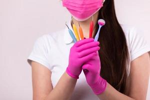 concepto de personas, medicina, odontología y salud - mujer dentista en mascarilla rosa y guantes médicos con herramientas de colores sobre fondo blanco. dentista para niños