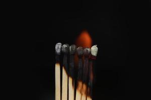 fósforos encendidos sobre fondo negro. fósforos encendidos en una fila de secuencia de quemado mientras un fósforo permanece alejado de la quema para evitar que el fuego se conecte contra un fondo negro.