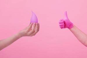 Hands of a young woman in pink latex gloves and hand with a menstrual cup on pink background. Women's health. Preservation of ecology. Waste-free use. Women's hygiene products. photo