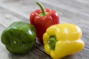 Red, green, and yellow pepper, on a wooden table. photo