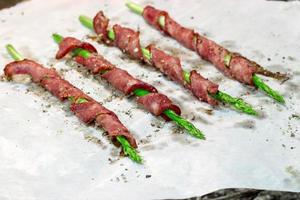 Asparagus wrapped in bacon with spices, grilled on paper for baking light background photo