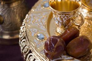 Still life with traditional golden Arabic coffee set with dallah, coffee pot, jezva, cup, and dates. Dark background. Horizontal photo