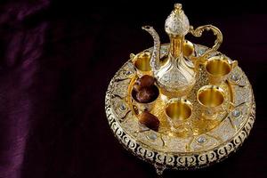 Still life with traditional golden Arabic coffee set with dallah, coffee pot, and dates. Dark background. Vertical photo