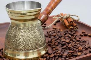 Copper coffee pot or ibrik with coffee beans and cinnamon sticks. On a wooden plate board. White background photo