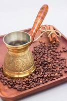 Copper coffee pot or ibrik with coffee beans and cinnamon sticks. On a wooden plate board. White background photo