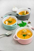 Three small serving pots or bowls with cream soup made of red lentils with rusks, spices and herbs parsley, and coriander. On a light gray background. photo