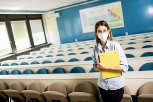 Female student wearing face protective medical mask for virus protection standing at lecture hall photo