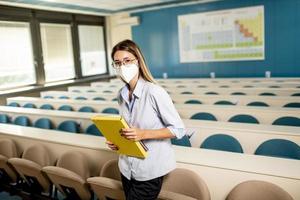 Female student wearing face protective medical mask for virus protection standing at lecture hall photo