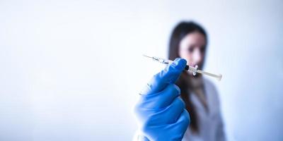 Enfermera irreconocible sosteniendo la vacuna con guante azul y fondo blanco con espacio para texto foto