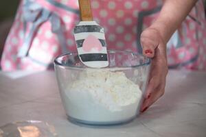 Woman mixing flour in a glass bowl with a pink apron at home photo