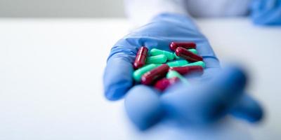 Enfermera mano llena de pastillas verdes y rojas con guante azul sobre fondo blanco.