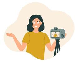 The blogger girl smiles and gestures in front of the camera, recording the video. Vector illustration in flat style