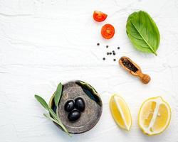 Fondo de alimentos con hierbas frescas, tomate, limón, pimienta negra, hojas de salvia, albahaca dulce y aceite de oliva sobre fondo de madera blanca foto