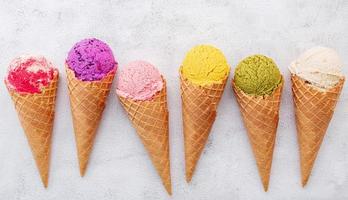 Varios de los sabores de helado en conos sobre fondo de piedra blanca foto