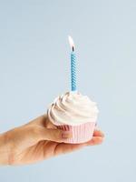 Hand holding delicious birthday cupcake on light blue background