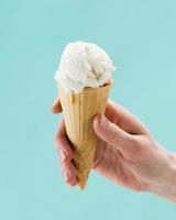 Mano sujetando el cono de helado de vainilla sobre fondo azul.