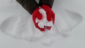 Young Woman in Winter Knitted Woolen Mittens Sculpts a Heart out of Snow