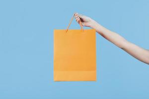 Hand holding a shopping bag on plain blue background