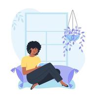 Young woman sitting by the window and reading a book, relaxing at home vector